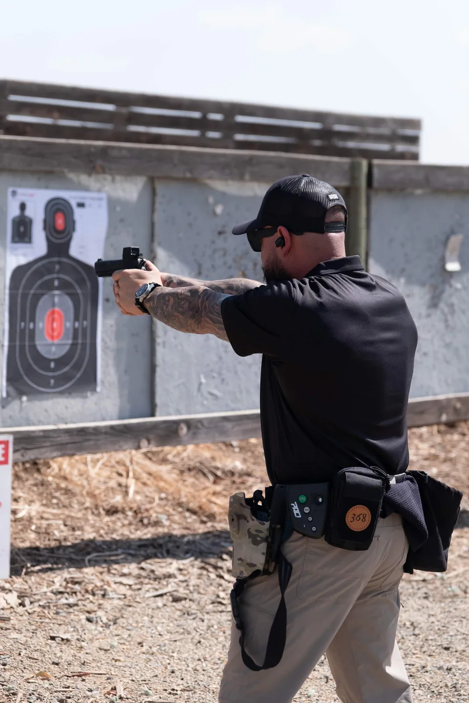 Silverline instructor firing a handgun two-handed at a black silhouette target on a steel backer, duty belt and magazine pouches on his hip.